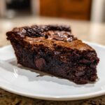 A decadent slice of hot fudge pie showing a dense, fudgy interior and melted chocolate chips.
