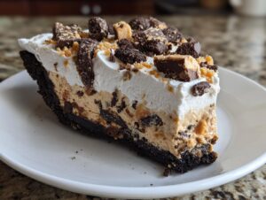 A thick slice of no-bake butterfinger pie with a dark chocolate crust, peanut butter filling, whipped topping, and candy pieces.