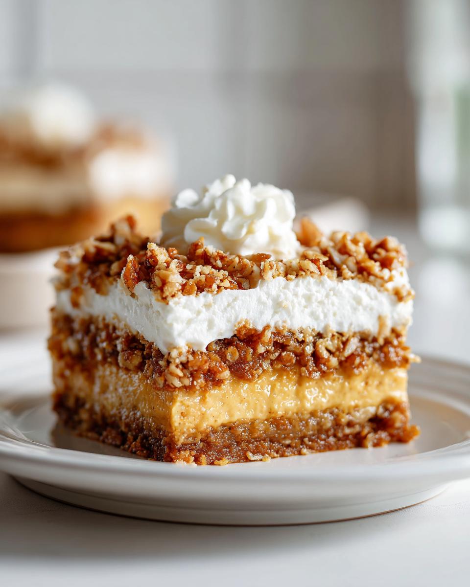 Close-up of a square slice of pumpkin crunch dessert showing layers of crust, pumpkin filling, whipped topping, and nuts.