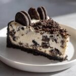 A close-up slice of creamy oreo cheesecake with a dark cookie crust, topped with crumbs and whole cookies.