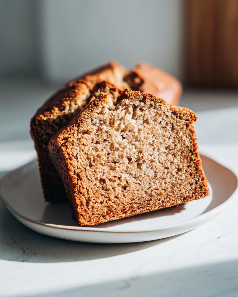 Two thick slices of moist Protein banana bread displayed on a small white plate, catching bright sunlight.