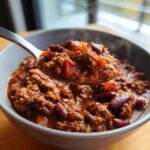 A spoonful of steaming, rich chili with ground meat and kidney beans, lifted from a bowl, showcasing the best chili recipe.