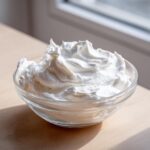 A clear glass bowl filled with perfectly stiff, bright white royal icing recipe mixture.