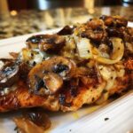 A close-up of juicy Texas Roadhouse smothered chicken topped with melted cheese, sautéed mushrooms, and onions.