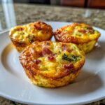 Three golden-brown Egg Muffin Cups filled with egg, ham, and spinach served on a white plate.