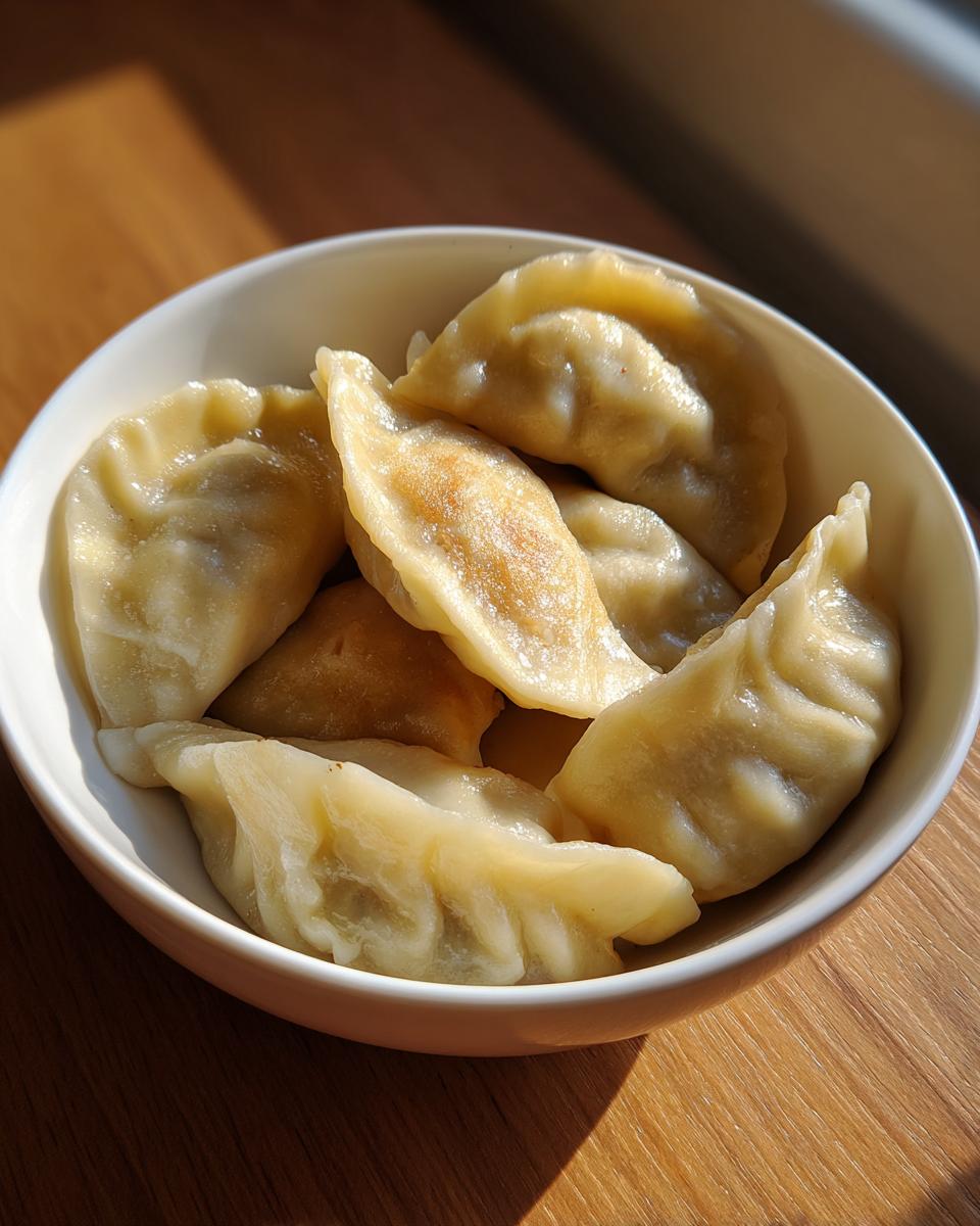A white bowl filled with freshly cooked Traditional Chinese Dumplings sitting on a wooden surface with bright sunlight.