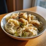 A close-up of pan-fried Traditional Chinese Dumplings served in a white bowl on a wooden table.
