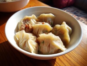 Close-up of several steamed Traditional Chinese Dumplings with visible meat filling in a white bowl.