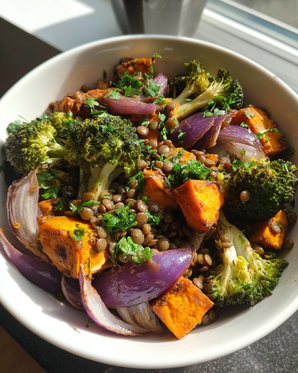 Close-up of a bowl containing a hearty veggie lentil salad with roasted sweet potatoes, red onion, and broccoli.