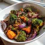 Close-up of a bowl of veggie lentil salad featuring brown lentils, roasted sweet potato, purple onion, and broccoli florets.