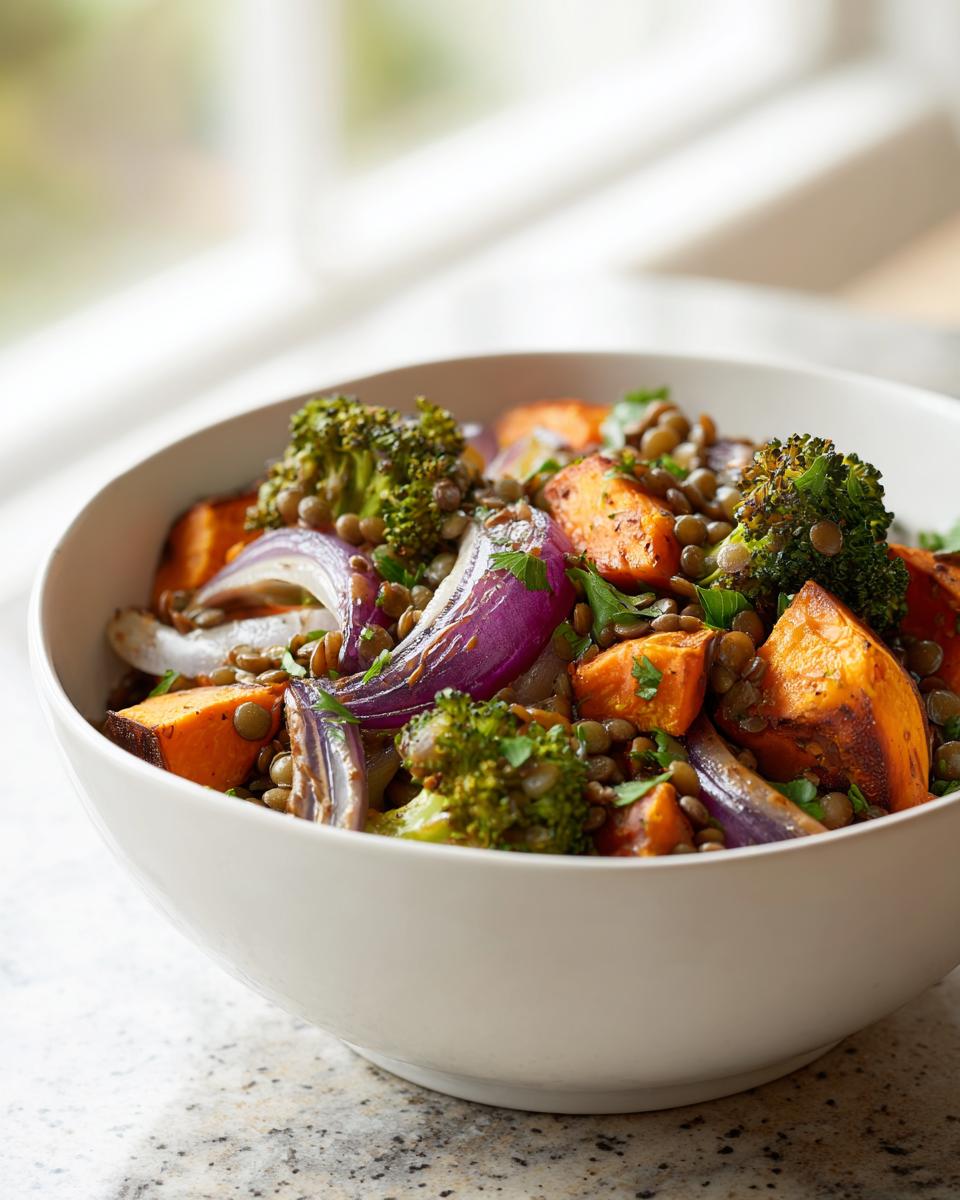 Close-up of a white bowl filled with veggie lentil salad featuring roasted sweet potatoes, red onion, and broccoli.