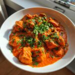 Close-up of creamy, vibrant orange butter chicken pieces garnished heavily with fresh chopped cilantro.