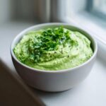 A creamy, vibrant green black bean dip served in a white bowl, garnished generously with fresh cilantro.