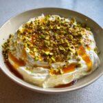 A bowl of creamy whipped feta dip topped with chopped pistachios and a drizzle of golden honey.