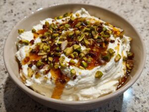 A creamy bowl of whipped feta dip topped generously with chopped pistachios, chili flakes, and drizzled honey.