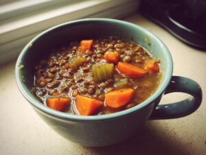 Close-up of a blue mug filled with thick, savory lentil soup featuring chunks of carrots and celery.
