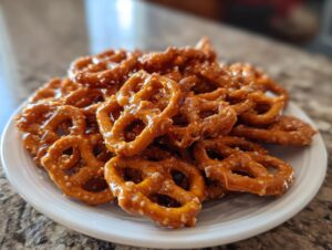 A close-up of a white plate piled high with shiny, glazed toffee pretzels, ready to eat.