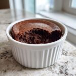 A close-up of a rich, dark chocolate mousse dessert served in a white fluted ramekin, showing a bite taken out revealing the creamy interior.