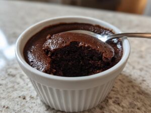 A spoonful being taken out of a rich, dark chocolate mousse served in a white fluted ramekin.