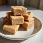 A tempting stack of creamy, light brown peanut butter fudge squares piled high on a small white plate.