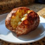 A fluffy, seasoned air fryer baked potato split open on a white plate, showing the soft interior.