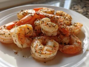 A close-up of perfectly cooked air fryer frozen shrimp seasoned with herbs on a white plate.