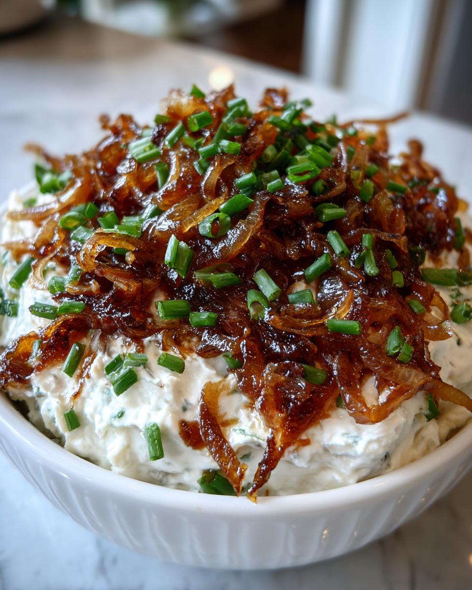 Close-up of creamy caramelized onion dip topped generously with dark caramelized onions and fresh chopped chives.