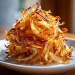A mound of golden brown, crispy caramelized onions piled high on a white plate.