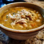 Close-up of a bowl filled with shredded chicken, white beans, and savory broth from the chicken chili recipe.
