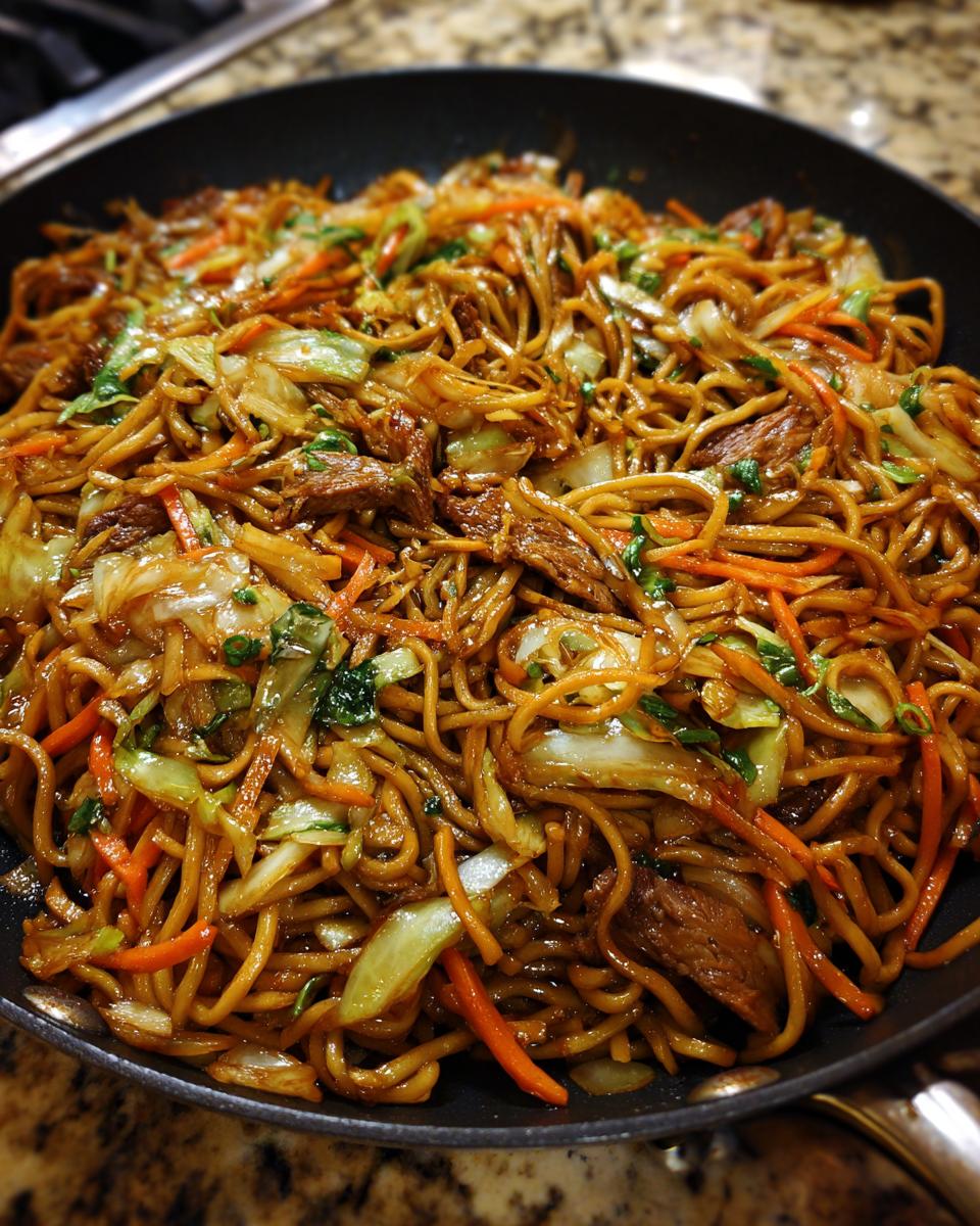 Close-up of savory beef and vegetable fried noodles coated in dark sauce, freshly cooked in a black skillet.