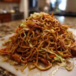 A large mound of glossy, dark brown fried noodles mixed with shredded cabbage and carrots, ready to serve.