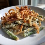 A serving of creamy green bean casserole topped generously with crispy fried onions.