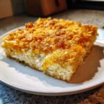 A square slice of amazing hot chicken salad with a creamy interior and crunchy, golden topping on a white plate.
