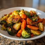 A close-up of beautifully caramelized roasted vegetables, including Brussels sprouts, carrots, and broccoli, seasoned with herbs.