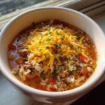 A hearty bowl of stuffed pepper soup topped with shredded cheddar cheese and fresh parsley.