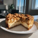 A rich slice cut from an apple pie cheesecake showing creamy filling, spiced apples, and a brown sugar crumble topping.
