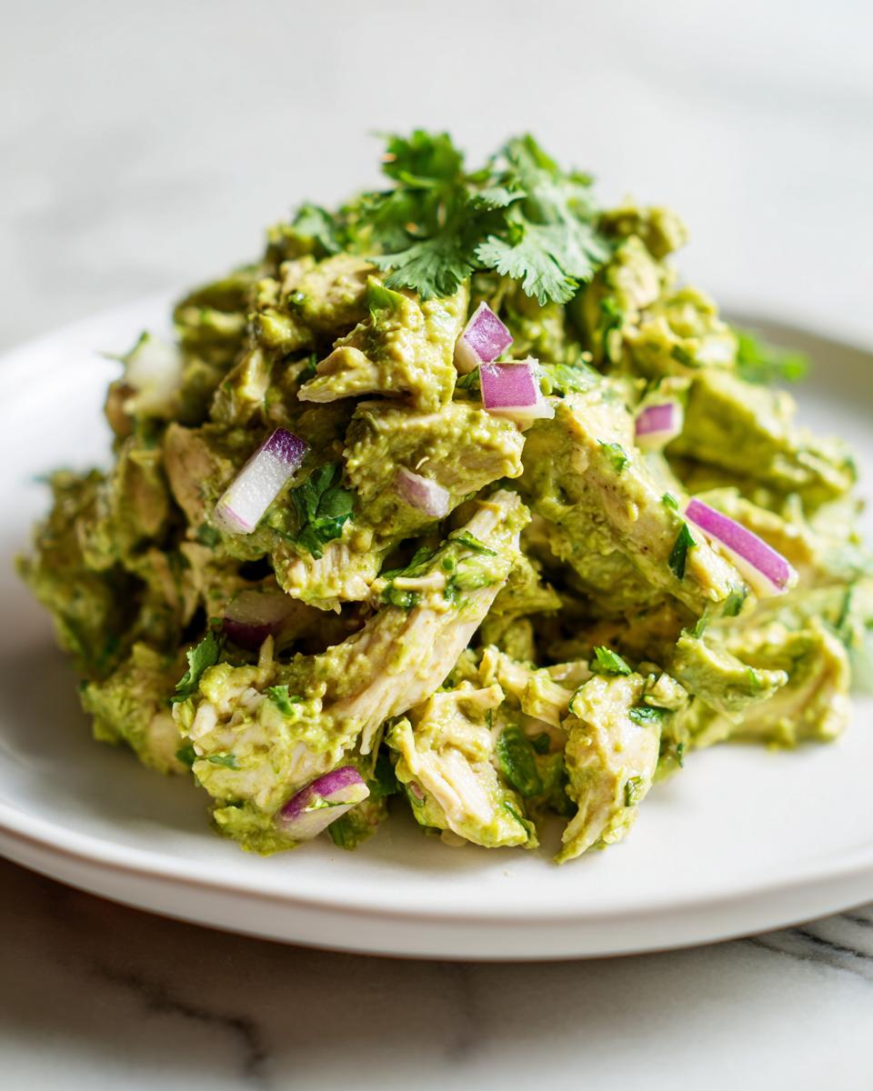 A mound of creamy avocado chicken salad mixed with chunks of chicken, red onion, and topped with fresh cilantro.