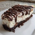 A decadent slice of Baileys Chocolate Cheesecake Trifle with a dark crust, white filling, and chocolate drizzle.