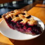 A close-up, sunlit slice of homemade blackberry pie featuring a juicy filling and a golden lattice crust.