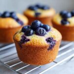 Close-up of a freshly baked blueberry protein muffins topped with fresh blueberries on a wire cooling rack.