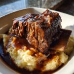 Close-up of incredibly tender braised short ribs served over mashed potatoes and covered in rich gravy.