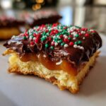 Close-up of a Caramel Ritz Cracker Christmas cookie square showing layers of cracker base, gooey caramel, chocolate, and festive sprinkles.