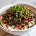 Close-up of a creamy caramelized onion dip topped generously with dark, rich caramelized onions and fresh green chives.