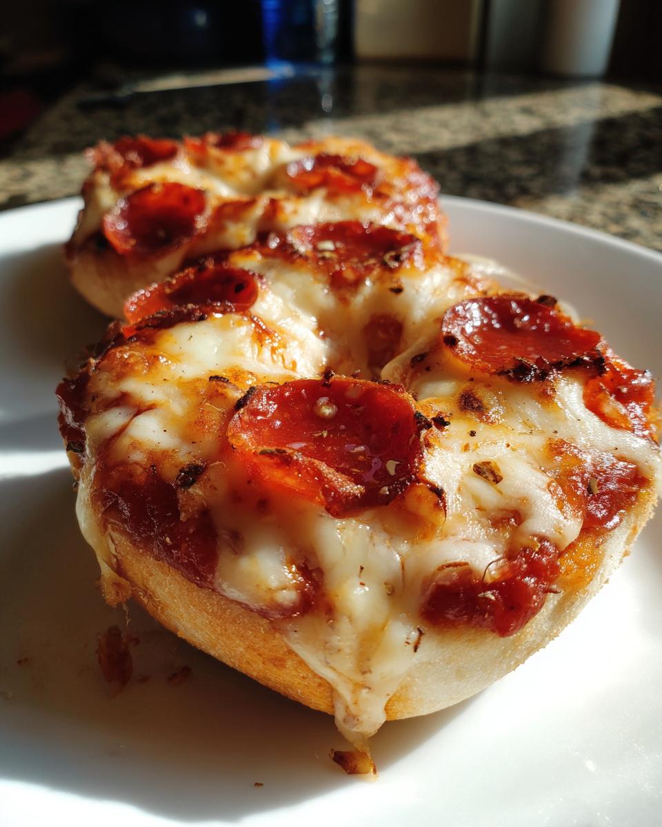 Close-up of two freshly baked pepperoni pizza bagels with melted, gooey cheese on a white plate.