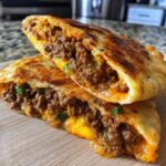 Two halves of a golden-brown baked cheesy pocket tacos, revealing a rich, seasoned ground beef and melted cheddar cheese filling.