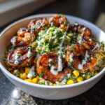 A close-up of a vibrant shrimp bowl featuring blackened chipotle lime shrimp, corn, rice, guacamole, and a white sauce drizzle.