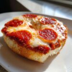 A close-up, appetizing shot of a single pepperoni pizza bagels half, topped with melted cheese and sauce.
