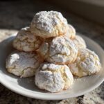 A stack of soft, crinkle-top cool whip cookies heavily dusted with powdered sugar on a white plate.