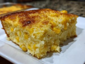 Close-up of a moist, golden slice of cream cheese corn casserole studded with bright yellow corn kernels.