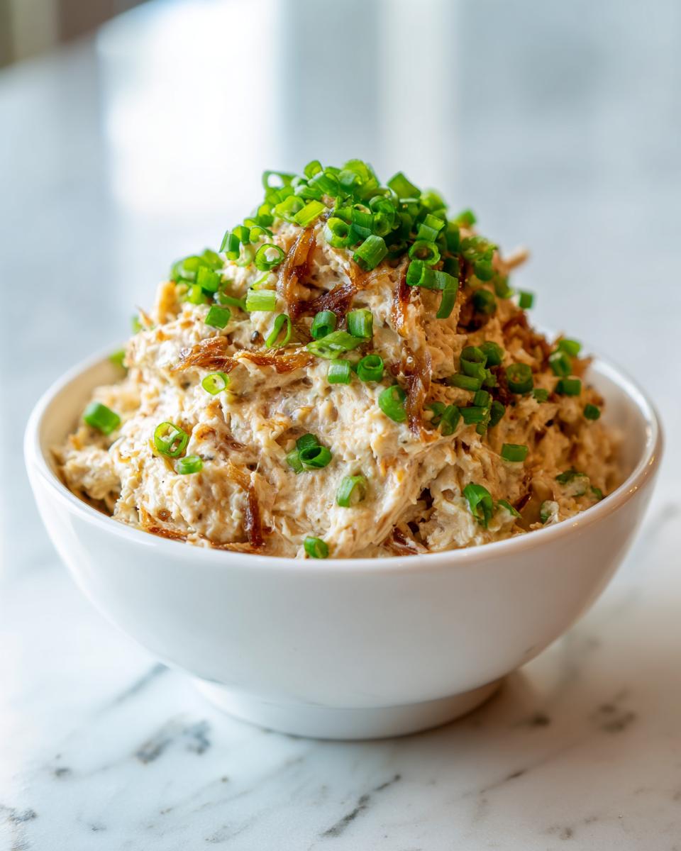 A bowl of creamy caramelized onion dip generously topped with crispy onions and fresh green chives.